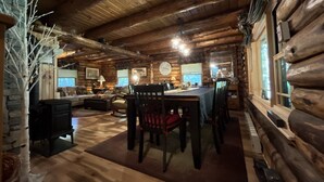 Interior de una cabaña de madera con comedor, chimenea y paredes de piedra.