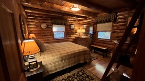 Un dormitorio tipo cabaña de madera con cama, lámparas de noche, un reloj, un aparador y una ventana.