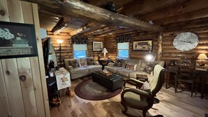 Interior rústico de una cabaña de troncos con sofá, sillón y comedor.
