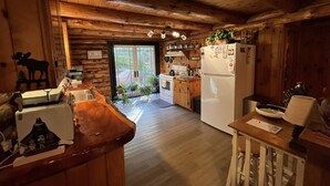 Interior de una cabaña de madera con cocina, comedor y un amplio ventanal.