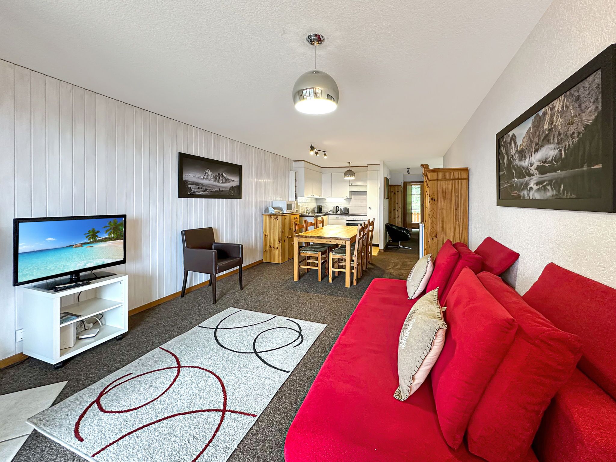 Una sala de estar moderna con televisor, sofá rojo y un comedor con mesa y sillas.