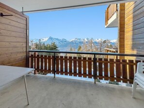 Ein Balkon mit Holzwertkasten, einem Tisch und Blick auf schneebedeckte Berge.