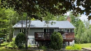 Une maison à deux étages dotée d’un balcon, entourée d’une pelouse bien entretenue et d’arbres.