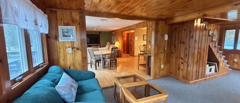 A wooden cabin interior with a sofa, a glass-top table, a staircase, and a dining area.