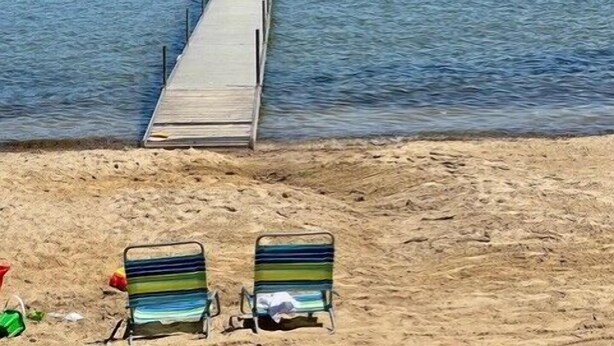 Une plage avec une jetée en bois qui s’avance dans un lac, le tout entouré de verdure.