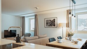 A modern hotel room with a kitchen area, a dining table, a sofa, and a large window with a view. - Alpine Apartments, (San Bernardino), by Interhome (San  Bernardino)