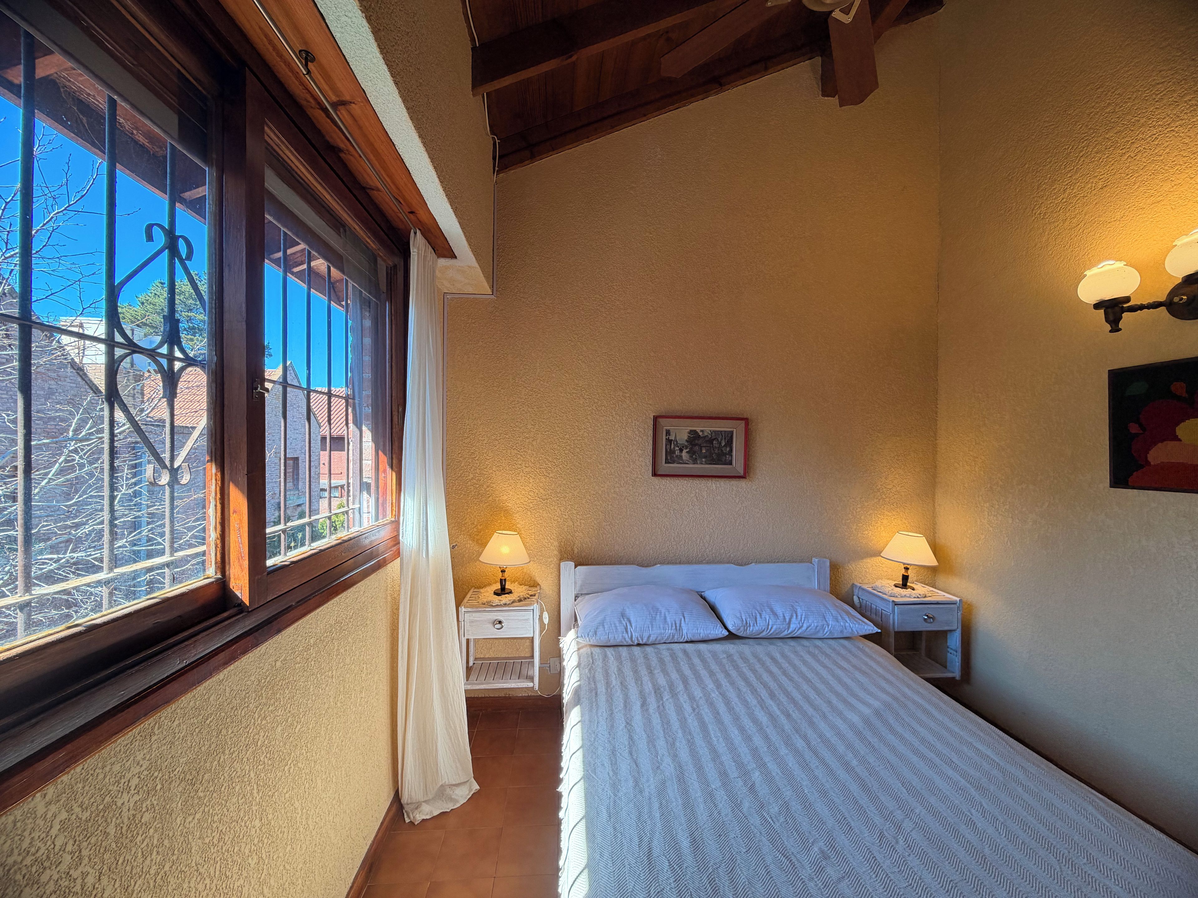 Una camera da letto con un letto, due comodini con lampade, una finestra con tende e un quadro appeso al muro.