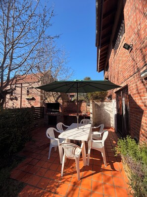 An outdoor patio with a brick wall, a table with chairs, and a green umbrella.