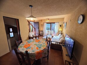 A dining area with a round table, chairs, a television, and a clock on the wall.