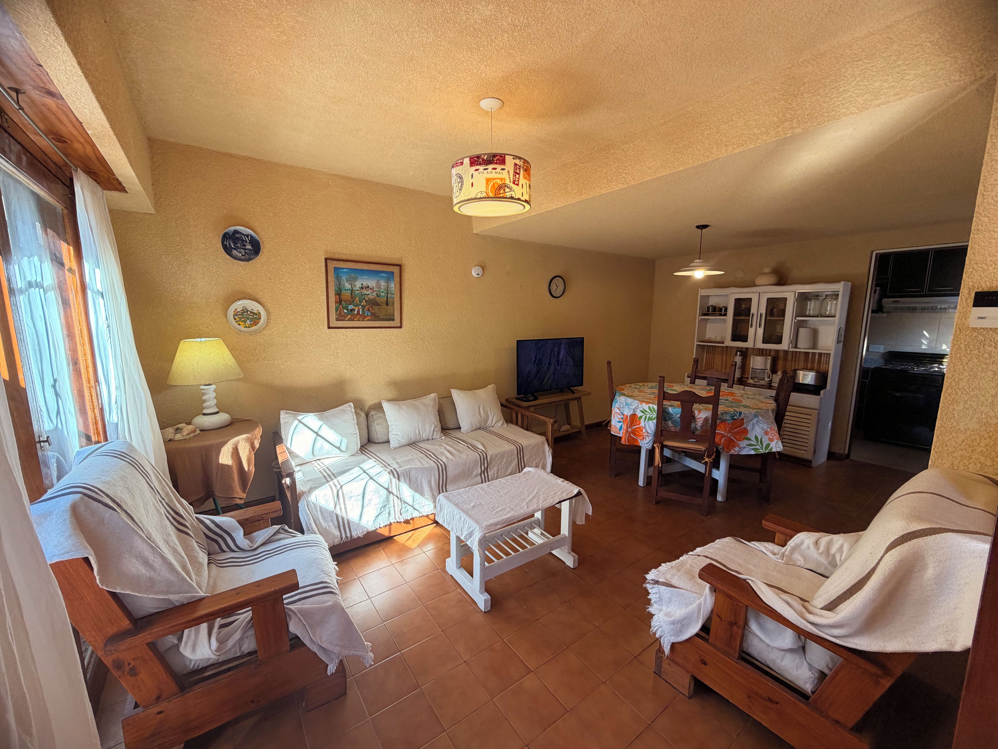 A cozy living room with a sofa set, a television, and a dining area with chairs and a table.