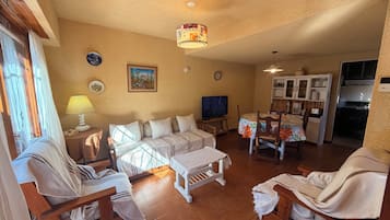 A cozy living room with a sofa set, a television, and a dining area with chairs and a table.