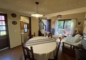 A room with a round dining table, a bed with a white bedspread, a TV, and a window with curtains.