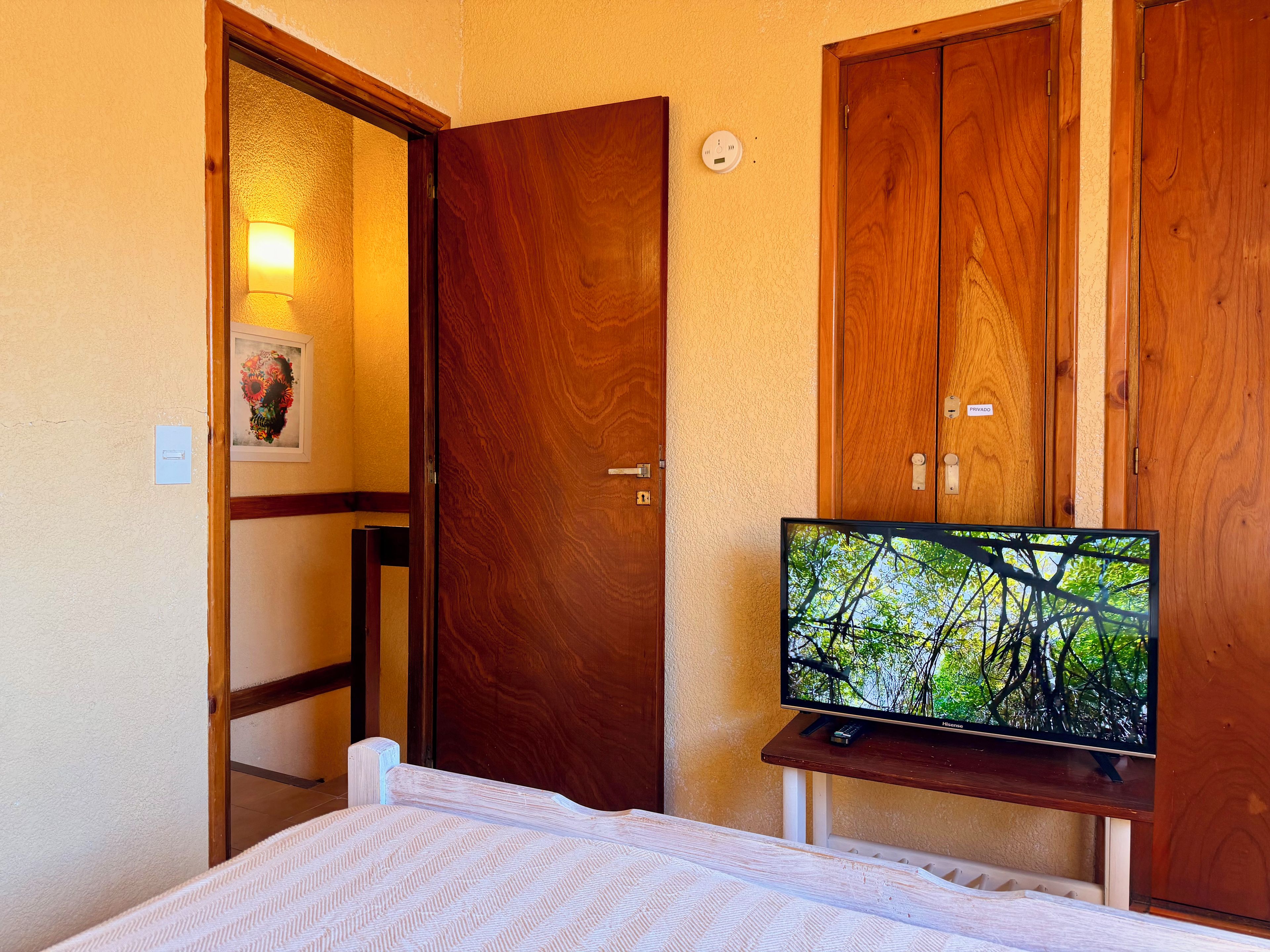 A hotel room with a bed, a television on a stand, wooden doors, and a wall-mounted light fixture.