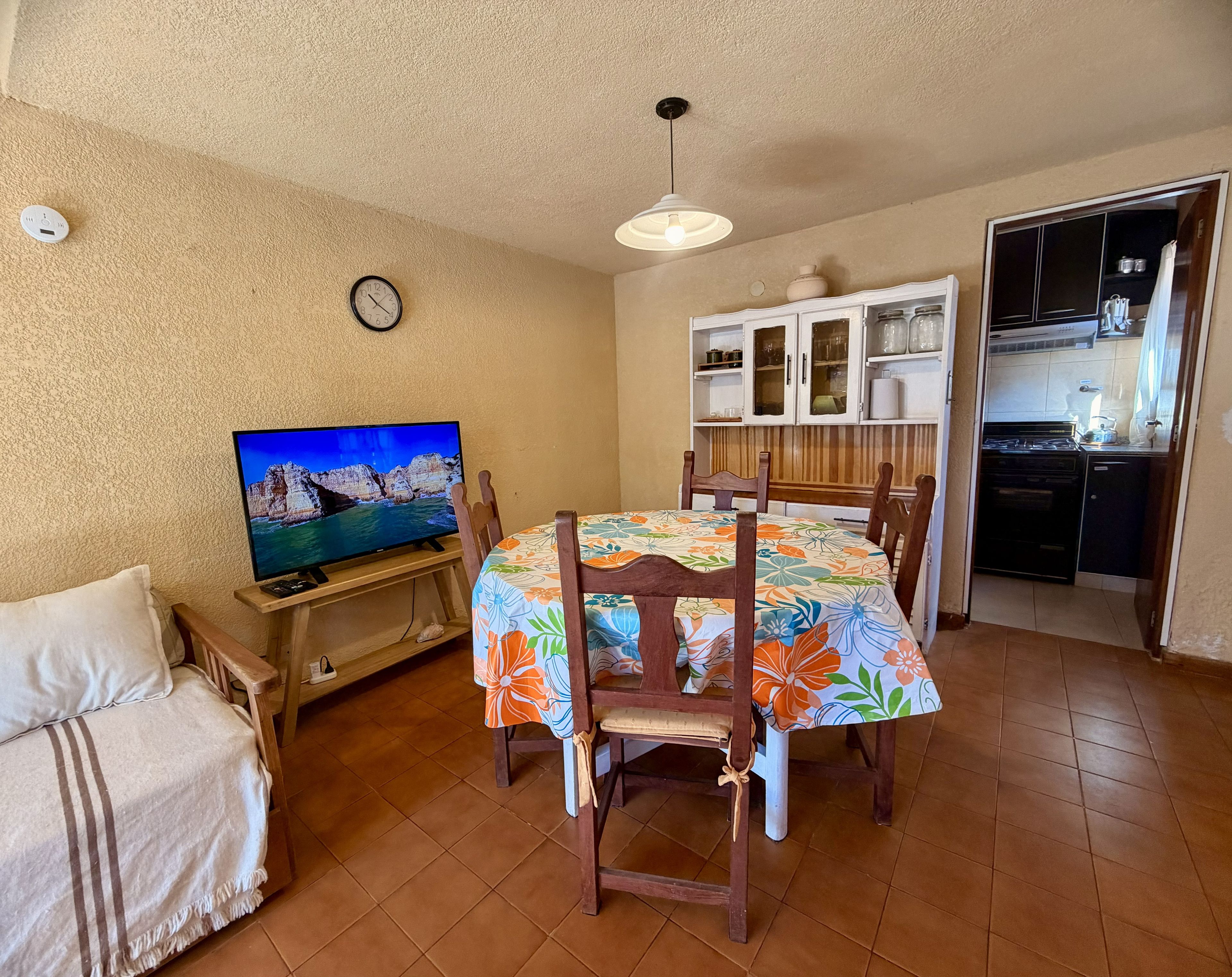 Uma sala de estar aconchegante com televisão, mesa de jantar com cadeiras, sofá e cozinha com armários e fogão.