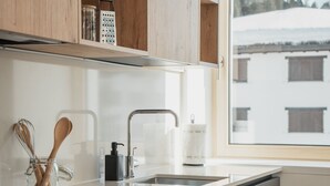Una cocina moderna con un lavamanos de acero inoxidable, armarios de madera, un ventanal con vistas a un paisaje nevado y una cafetera.
