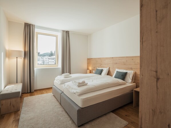 Une chambre d’hôtel moderne avec un grand lit, une table de chevet, une lampe et une vue sur les bâtiments par la fenêtre.