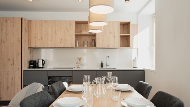 Una cocina moderna con armarios de madera, una mesa de comedor con platos y vasos, e iluminación colgante.
