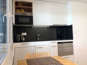 A compact kitchen with white cabinets, a black countertop, and a wooden dining table. - Plein coeur de Nendaz by Interhome (Nendaz)