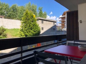 A balcony with a red table and chairs, a view of trees and buildings, and a railing. - Plein coeur de Nendaz by Interhome (Nendaz)