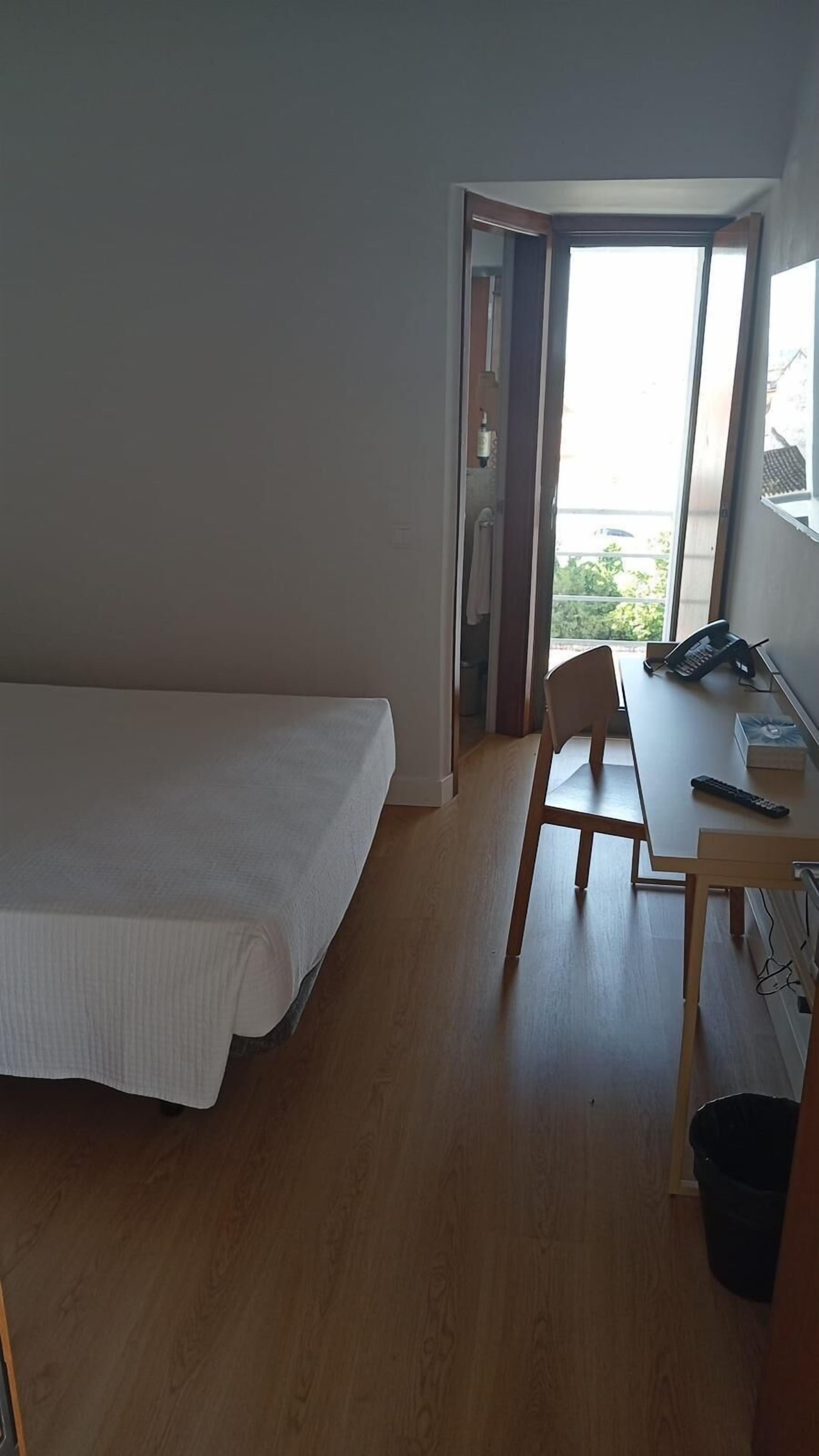 A room with a bed, a desk, a chair, a telephone, and a window.