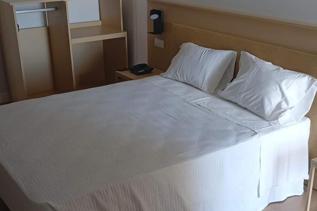 A neatly made bed with a wooden headboard, a bedside table with a lamp, and a wall-mounted device.