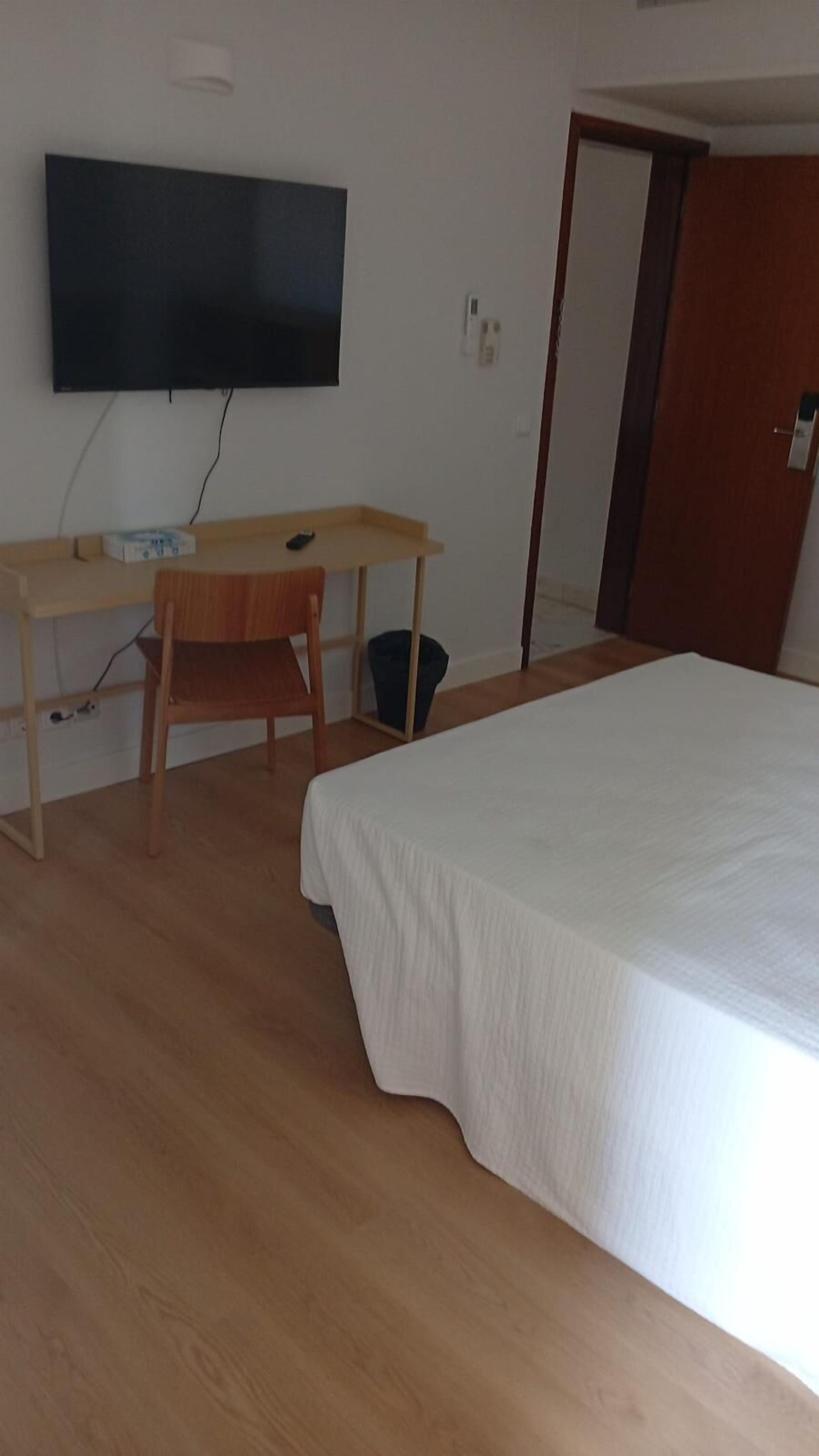 Un dormitorio con cama, escritorio, silla, televisor y puerta.