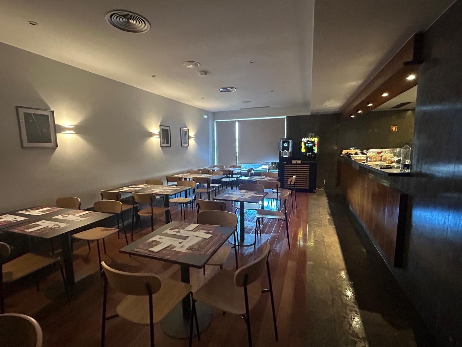A restaurant with tables and chairs, a counter with a display case, and wall-mounted lights.
