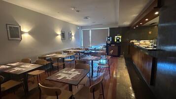 A restaurant with tables and chairs, a counter with a display case, and wall-mounted lights.