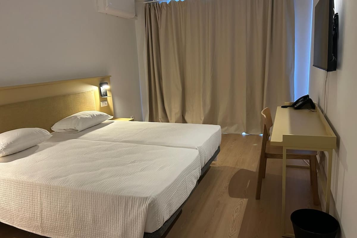 A hotel room with two beds, a desk, a chair, a TV, and a trash bin.