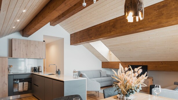 Una cocina moderna con armarios de madera, un comedor con una mesa de madera lista para una comida, y un dormitorio tipo loft con un sofá gris.