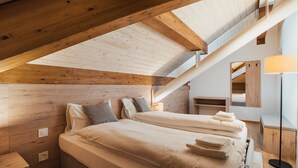 Un dormitorio con techo inclinado, vigas de madera, una cama con almohadones, una mesita de noche, una lámpara y un espejo.