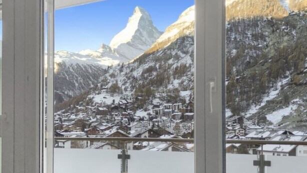 A window with a view of a snowy mountain landscape, including a prominent peak and a village below.