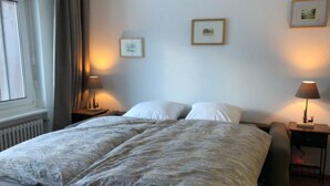 A bed with a grey blanket, two bedside tables with lamps, and two framed pictures on the wall.