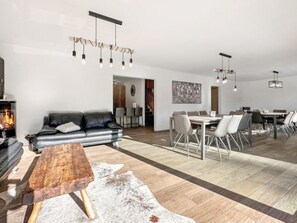 Un salon moderne avec une cheminée, un coin repas et une cuisine en arrière-plan.