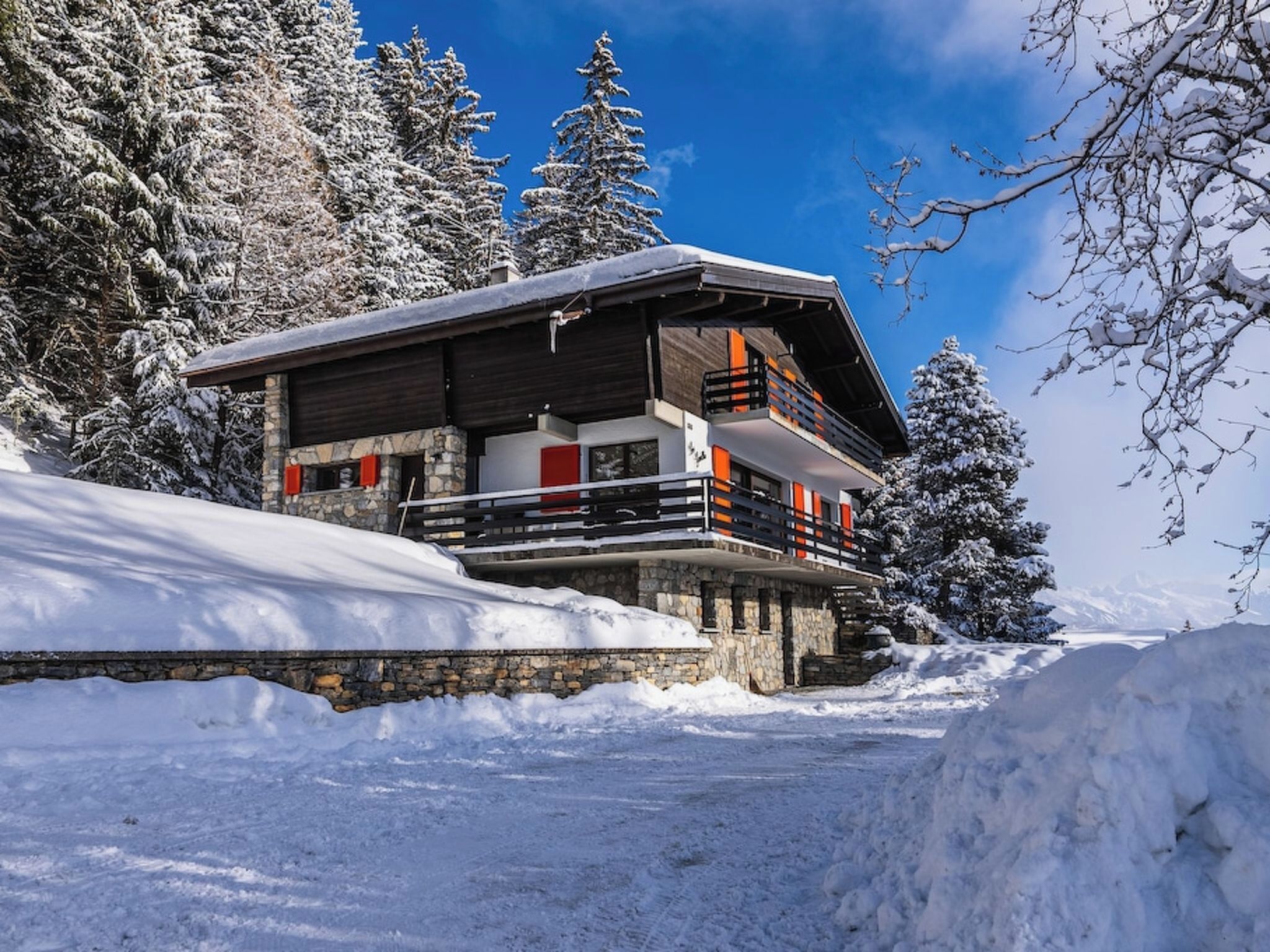 A snow-covered lodge with a stone foundation, wooden upper structure, and a balcony with orange railings.