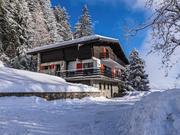 A snow-covered lodge with a stone foundation, wooden upper structure, and a balcony with orange railings.