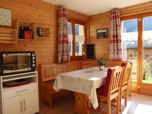 A wooden cabin interior with a dining table, chairs, a microwave, and a small kitchen area. - Petit Nid Douillet au Coeur de Salvan by Interhome (Salvan)