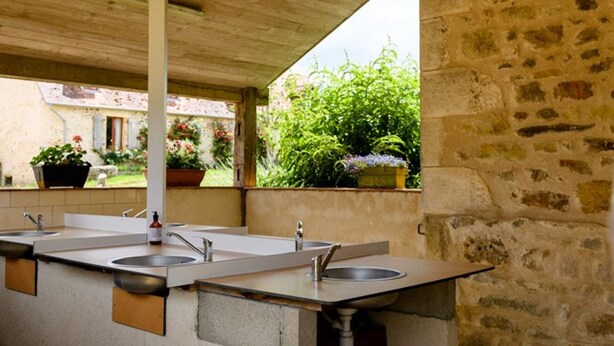 Un espacio al aire libre techado con pared de piedra, techo de madera y un largo banco con lavamanos.