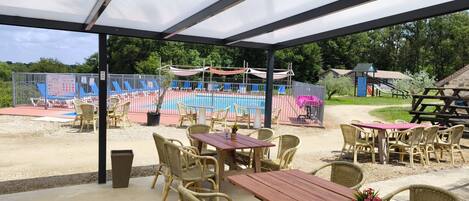 An outdoor patio area with tables and chairs, a covered seating area, and a playground in the background.