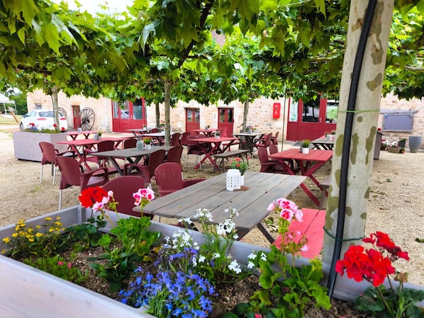 An outdoor seating area with tables and chairs, surrounded by flowering plants and trees.