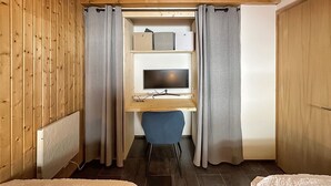 Une pièce de taille modeste avec un plafond en bois, un bureau avec un ordinateur, une chaise et un lit recouvert d’une housse blanche.