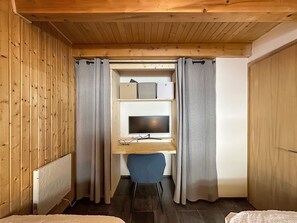 Ein kleines Zimmer mit Holzbalkendecke, einem Schreibtisch mit Computer, einem Stuhl und einem Bett mit weißer Bettdecke.