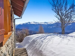 Eine Holzhütte mit Steinfassade, verschneitem Gelände und Blick auf die Berge.