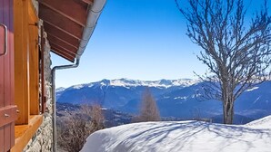 Une cabane en bois avec un mur en pierre, une pente enneigée et une chaîne de montagnes en arrière-plan.