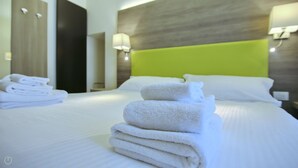 A hotel room with a neatly made bed, a stack of folded towels, and a bright green headboard. - Affittacamere Brenna (San Fermo della Battaglia)