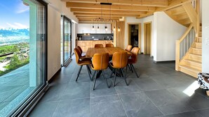 Una cocina moderna con vigas de madera, un comedor con una mesa grande y sillas, y vistas a un paisaje a través de amplios ventanales.