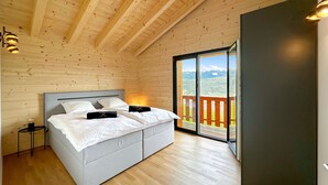 Un dormitorio con una cama grande, vigas de techo de madera, una mesita de noche y vistas a una terraza exterior por medio de una puerta de cristal.