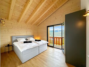 A bedroom with a large bed, wooden ceiling beams, a nightstand, and a view through a glass door to an outdoor deck. - My Mountain Paradise in the Swiss Alps by Interhome (Grône-Loye)