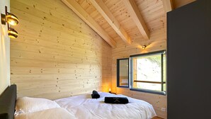Un dormitorio tipo cabaña de madera, con cama, almohadas, una lámpara de noche y una ventana.