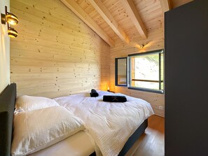 A wooden cabin bedroom with a bed, pillows, a bedside lamp, and a window. - My Mountain Paradise in the Swiss Alps by Interhome (Grône-Loye)
